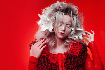 Shades of red. Strange attractive woman in a red outfit, on a red background, with lily flowers in...