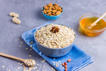 Dry oatmeal, nuts and honey. Oatmeal and almond nuts on cement background. Cereal and peanuts for making healthy breakfast. Oatmeal in bowl on blue napkin