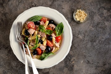 Salad with canned tuna, pasta, cherry tomatoes, olives, parmesan, olive oil and basil. Top view. 