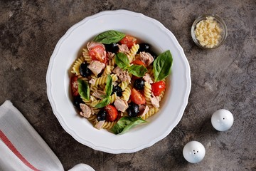 Salad with canned tuna, pasta, cherry tomatoes, olives, parmesan, olive oil and basil. Top view. 