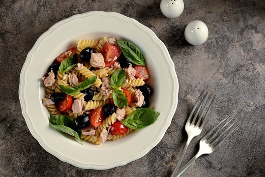Salad with canned tuna, pasta, cherry tomatoes, olives, parmesan, olive oil and basil. Top view. 