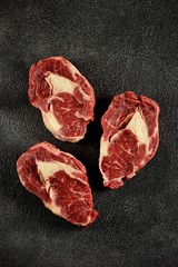 Obraz premium Three raw fresh beef steaks rib eye on a black background. Top view. Copy space. 
