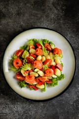 Healthy potato gnocchi salad with cherry tomatoes, cucumber, bell pepper, slightly salted salmon, olive oil and lettuce. Top view. 