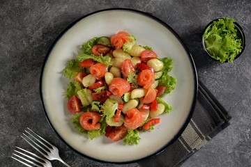 Healthy potato gnocchi salad with cherry tomatoes, cucumber, bell pepper, slightly salted salmon, olive oil and lettuce. Top view. 