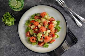 Healthy potato gnocchi salad with cherry tomatoes, cucumber, bell pepper, slightly salted salmon, olive oil and lettuce. Top view. 