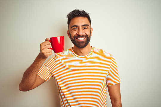 Young indian man drinking red cup of coffee standing over isolated white background with a happy face standing and smiling with a confident smile showing teeth