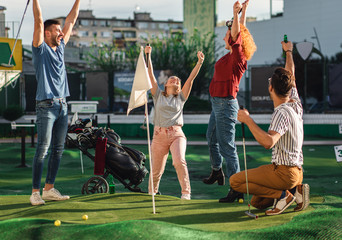 Group of smiling friends enjoying together playing mini golf in the city. - obrazy, fototapety, plakaty