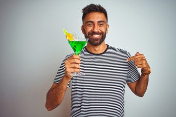 Young indian man drinking cocktail with alcohol standing over isolated white background with surprise face pointing finger to himself