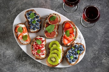 Healthy vegetarian sandwiches made from rye bread with soft cheese, organic berries and fruits - strawberries, blueberries, kiwi, figs, pomegranate seeds and mint.