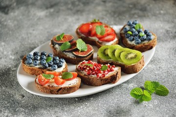Healthy vegetarian sandwiches made from rye bread with soft cheese, organic berries and fruits - strawberries, blueberries, kiwi, figs, pomegranate seeds and mint.