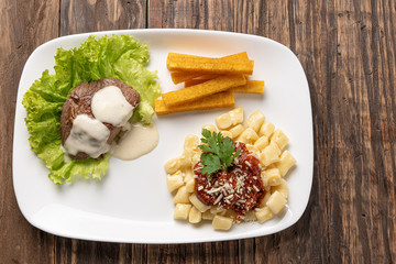 Homemade gnocchi pasta with tomato sauce and beef mignon with cheese sauce in a white plate on wooden  background