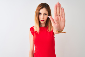 Fototapeta premium Redhead businesswoman wearing elegant red dress standing over isolated white background doing stop sing with palm of the hand. Warning expression with negative and serious gesture on the face.