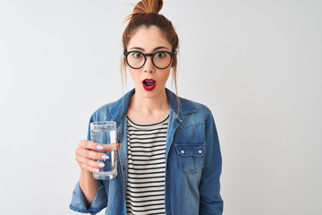 Young beautiful redhead woman drinking glass of water over isolated white background scared in...