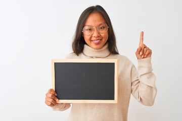 Young chinese woman wearing glasses holding blackboard over isolated white background surprised with an idea or question pointing finger with happy face, number one