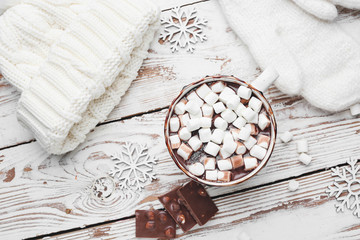 Cup of hot chocolate with marshmallows, knitted hat and mittens on white wooden background