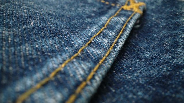 Extreme detailed of blue denim jeans cloth texture in macro dolly shot over the cloth surface. Flow view of clothing material. Textile abstract background. Vintage fashion apparel industry concept.