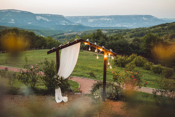 Wooden wedding arch with white cloth and light bulbs outdoors with amazing mountain view on...