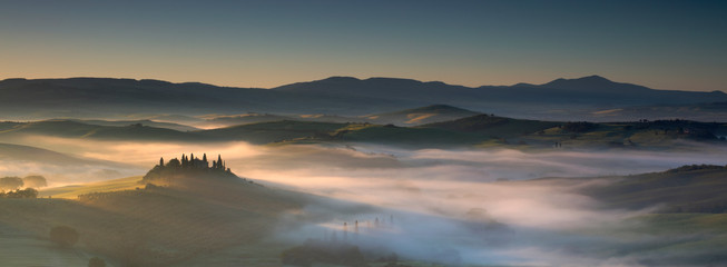Misty dawn over farmhouses vineyards olive groves San Quirico Val D'Orcia Tuscany Italy