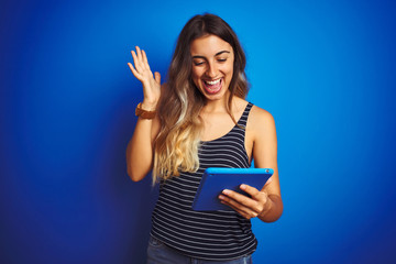Young beautiful woman using touchpad tablet over blue isolated background very happy and excited,...