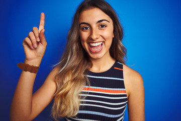 Young beautiful woman wearing stripes t-shirt over blue isolated background surprised with an idea or question pointing finger with happy face, number one