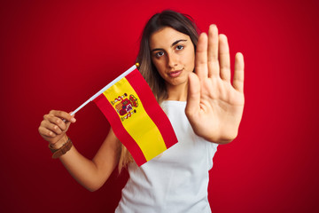 Young beautiful woman holding spanish flag over red isolated background with open hand doing stop sign with serious and confident expression, defense gesture