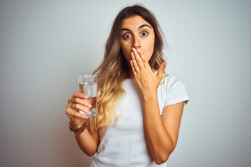 Young beautiful woman drinking a glass of water over white isolated background cover mouth with hand shocked with shame for mistake, expression of fear, scared in silence, secret concept