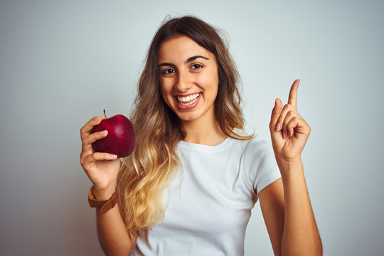 Young beautiful woman eating red apple over grey isolated background very happy pointing with hand and finger to the side