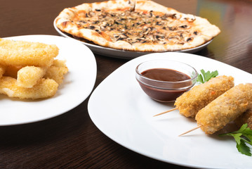 Korndog on skewers, and cheese sticks. Pizza. On the plates.