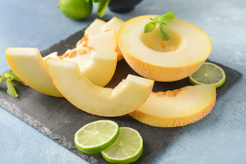 Slate plate with tasty melon and lime on color background