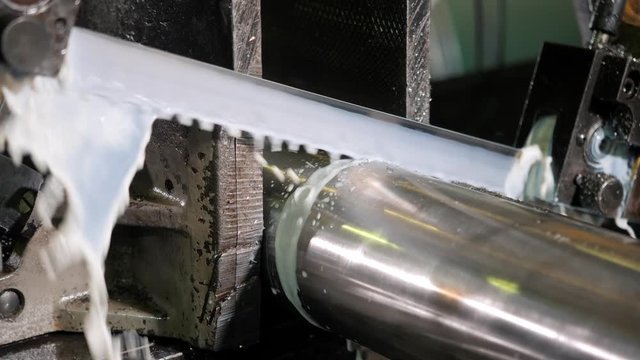 The industrial sawing machine cutting the material rod. The band saw machine cutting raw metals rods the with the coolant fluid.