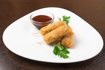 Korndog on skewers, breaded and with sauce. On the plate.