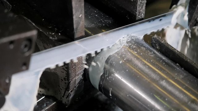The industrial sawing machine cutting the material rod. The band saw machine cutting raw metals rods the with the coolant fluid.