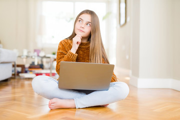 Beautiful young girl studying using laptop sitting on the floor at home serious face thinking about question, very confused idea