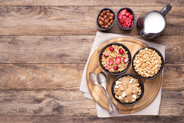 Breakfast cereals in bowls with a jug of milk on rustic wooden table, top view with copy space