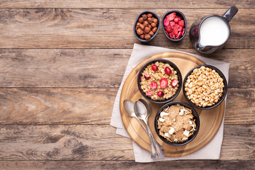 Breakfast cereals in bowls with a jug of milk on rustic wooden table, top view with copy space