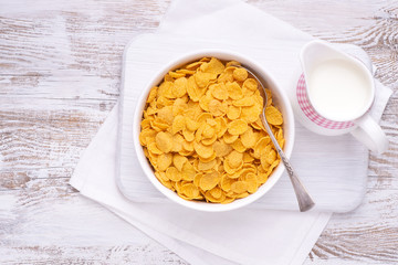 Cornflakes in a white bowl with jug of milk on a rustic wooden table, top view with copy space