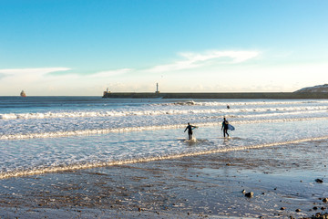 Fototapeta na wymiar A couple of surfers enter water on Aberdeen beach near South breakwater, Scotland