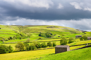 Bright sun with dark clouds over Swaledale drystone walls and barns near High Oxnop Hall Gunnerside Richmond England