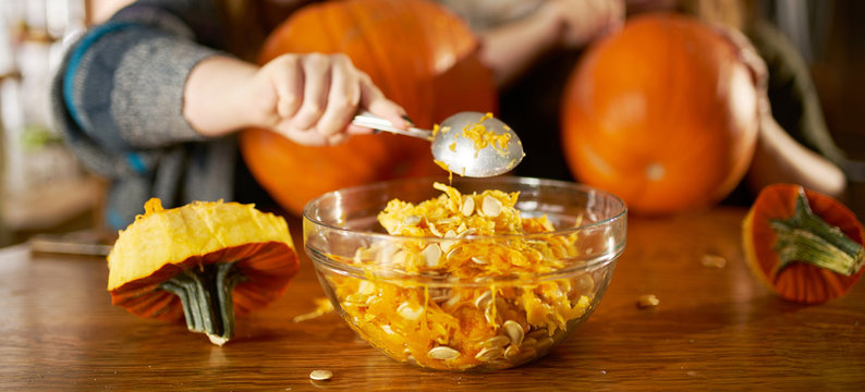 family fun activity for halloween- two sisters removing insides of pumpkin and placing it inside bowl with focus on spoon