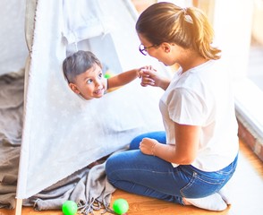 Beautiful teacher and toddler boy sitting on the floor playing inside  tipi at kindergarten