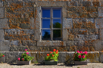 Fototapeta na wymiar Le vieux mur de pierres, la vieille fenêtre et les trois pots fleuris, département de la Haute-Loire en région Auvergne-Rhône-Alpes, France 