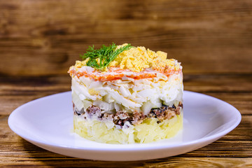 Plate with traditional russian salad Mimosa on a wooden table. Layered salad with potatoes, sardine, cheese, carrot, eggs and mayonnaise