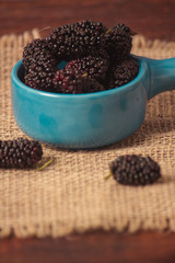 Fresh blackberries on wooden table in a blue bowl with a rustic jute.