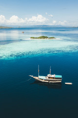 Luxus-Kreuzfahrtboot, das in der Nähe der Korallenriff-Atollinsel mit atemberaubendem weißen tropischen Strand und Bergen am Horizont segelt. Luftaufnahme. Luxus-Meeresreise- und Urlaubskonzept.