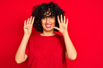 Young arab woman with curly hair wearing casual t-shirt over isolated red background showing and...