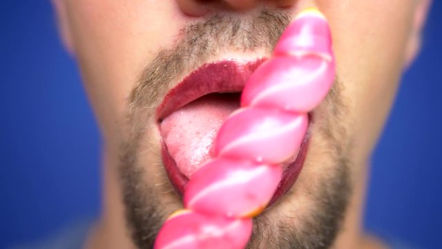 close-up, bearded man with painted lips eats a lollipop.