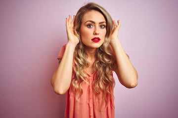 Young beautiful woman wearing t-shirt standing over pink isolated background Trying to hear both hands on ear gesture, curious for gossip. Hearing problem, deaf