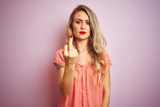 Young beautiful woman wearing t-shirt standing over pink isolated background Showing middle finger, impolite and rude fuck off expression