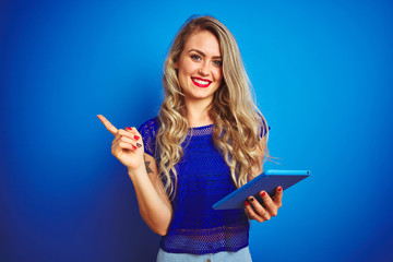 Young beautiful woman using tablet over blue isolated background very happy pointing with hand and...