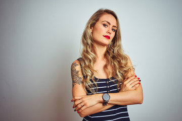 Young beautiful woman wearing stripes t-shirt standing over white isolated background looking to the side with arms crossed convinced and confident